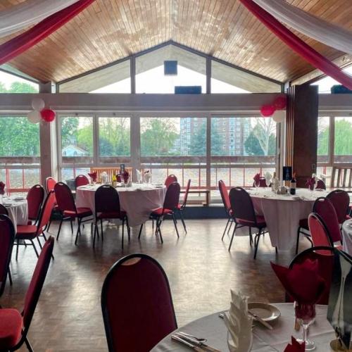 A large event space with wooden floors and ceilings. A balcony can be seen out the windows overlooking the River Thames. There are tables and chairs arranged in the room, with red and white drapes coming from a mirror ball in the centre of the ceiling.