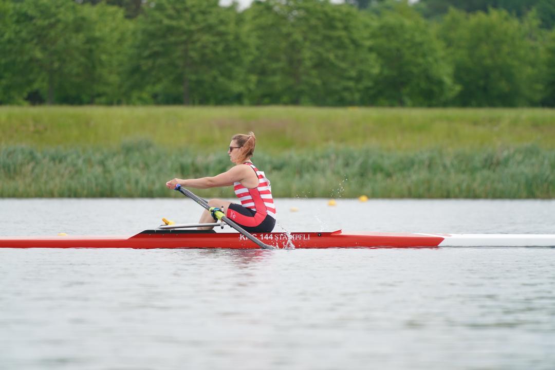 A woman in a single scull rowing boat wearing a red and white striped unisuit