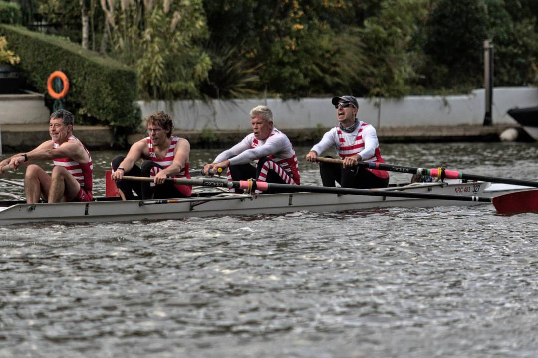 Four men in a rowing boat during a head race. They are wearing red and white striped kit, and the oars have red spoons.